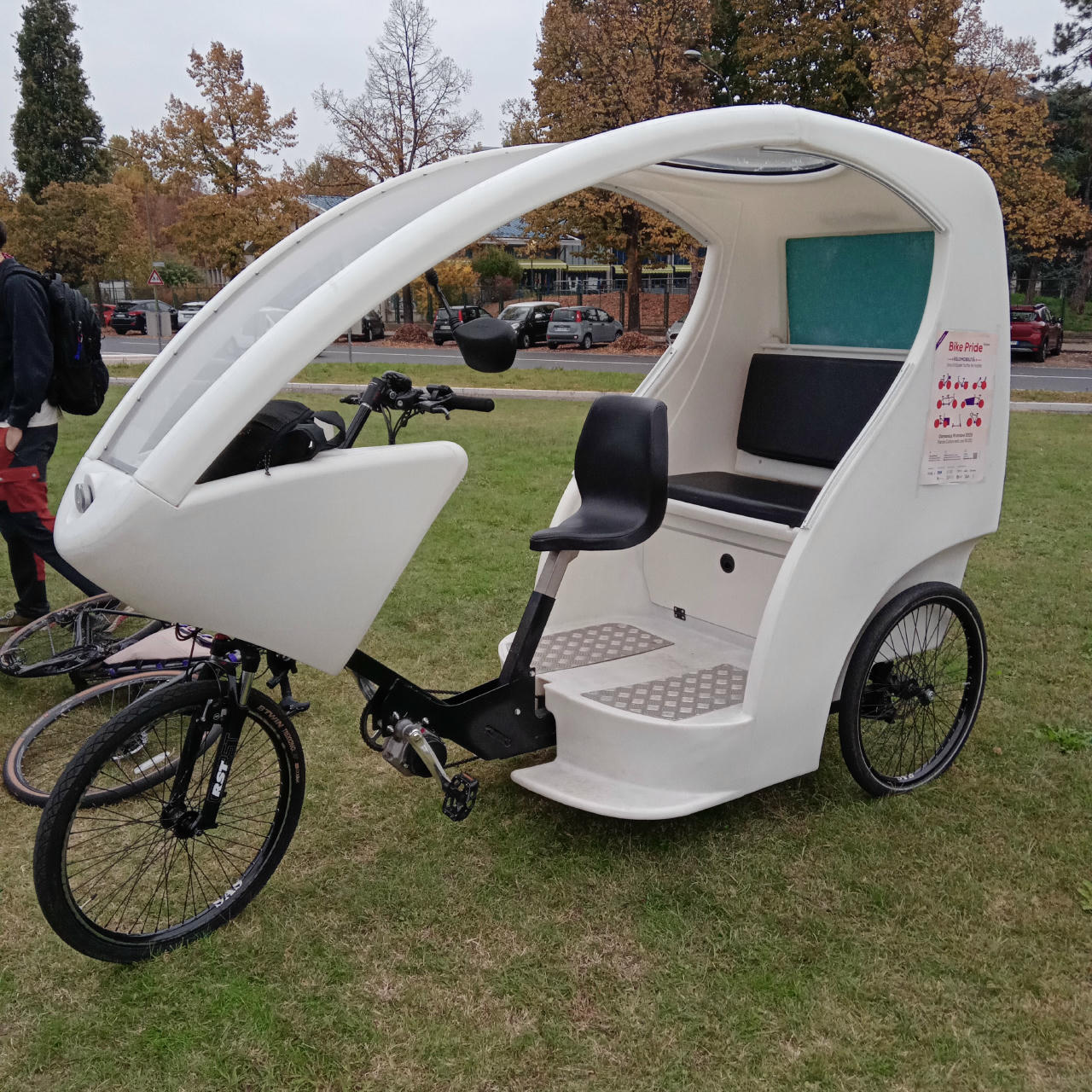 Un "rikisho" a pedalata assistita, con due posti oltre a chi pedala, tutti coperti da eventuale pioggia. Sul fianco è appeso il volantino dell'iniziativa "Bike Pride".