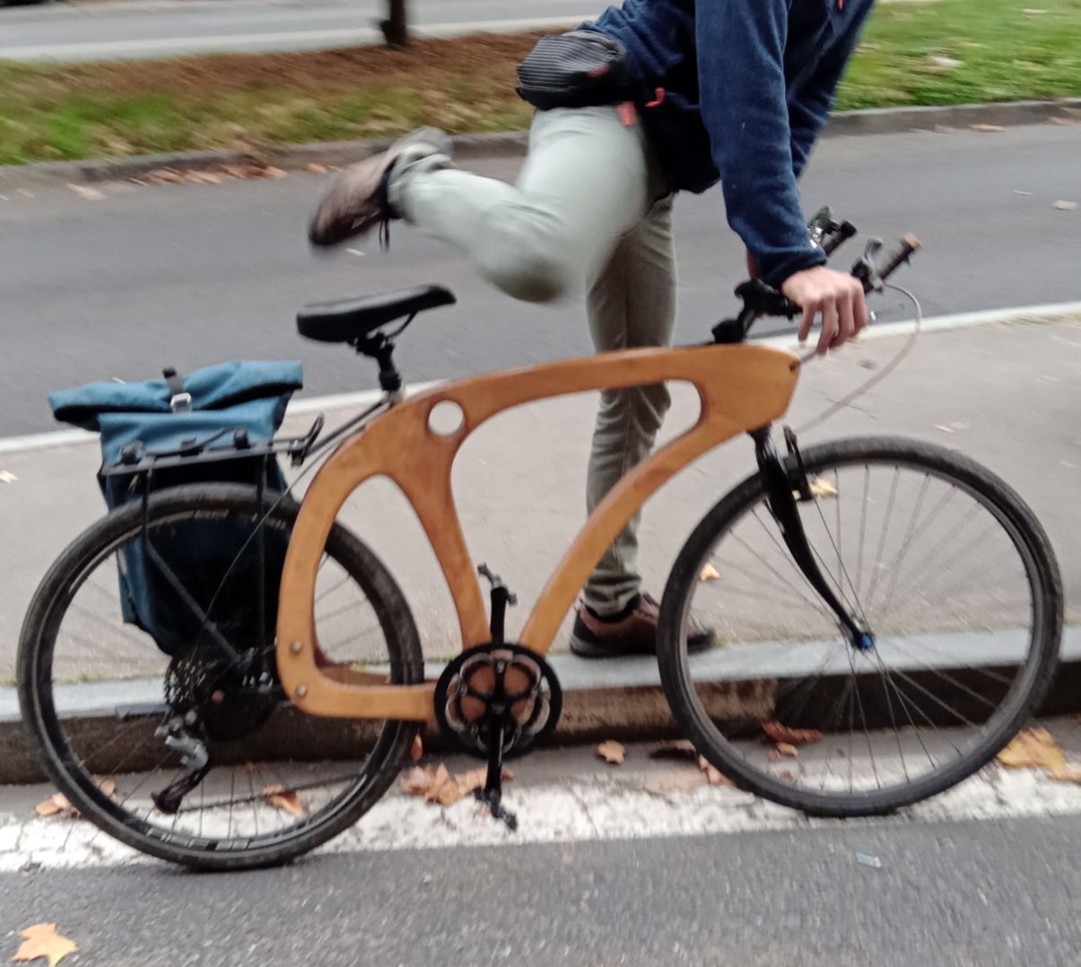 A bordo strada una persona scende da una bicicletta con il telaio in legno.