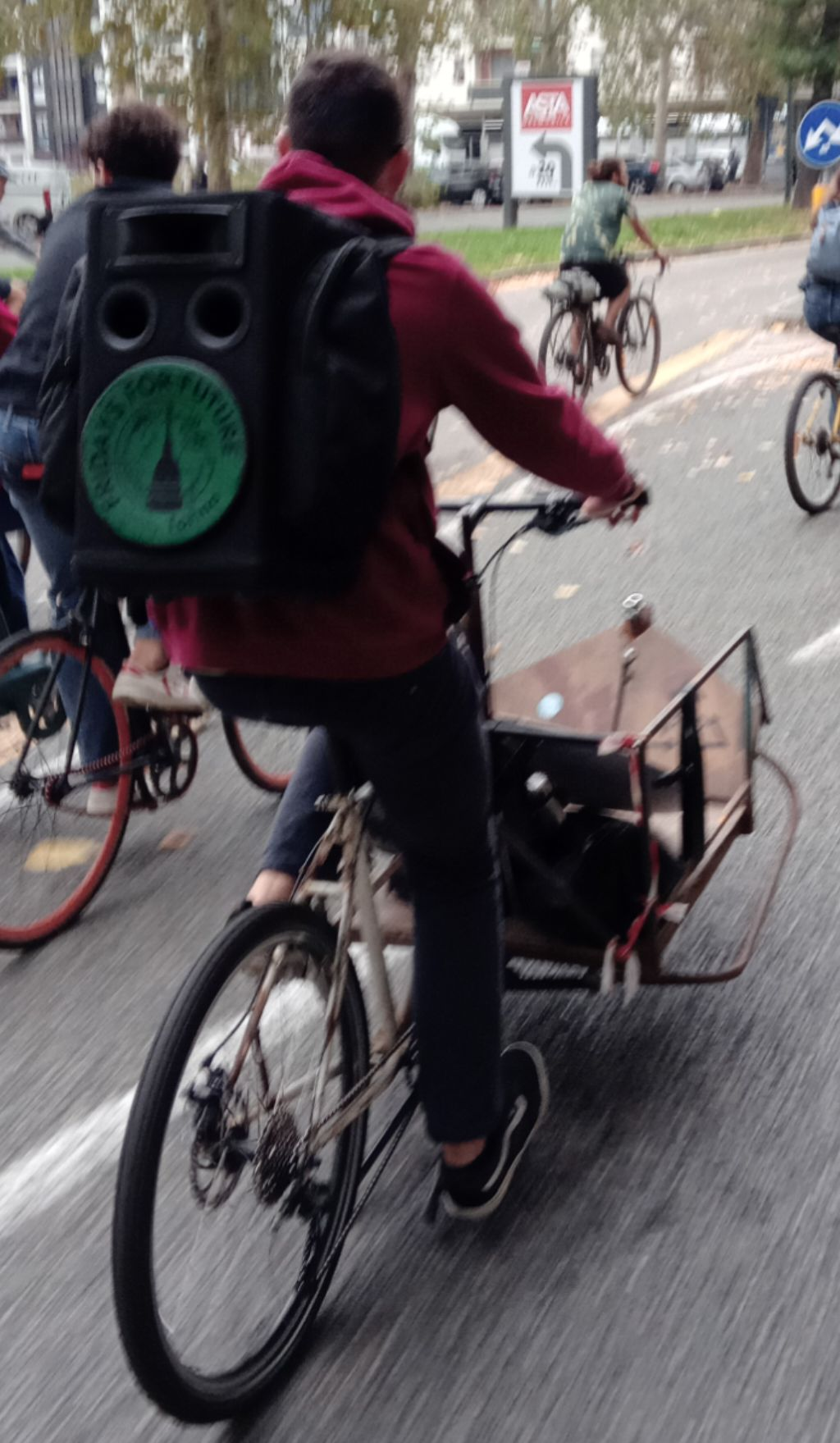 Una persona pedala con una bici cargo, portando sulle spalle una cassa acustica con il logo verde di Fridays for Future - Torino